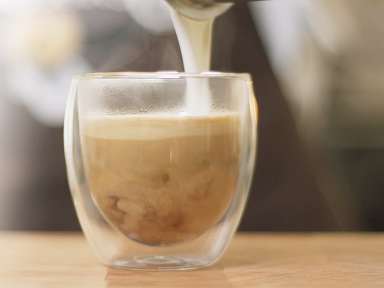 Cappuccino die gezet wordt in een doorzichtig glas.